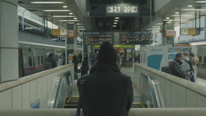A person with their back turned is standing in warm black clothes and looking straight ahead where they are in a terminal