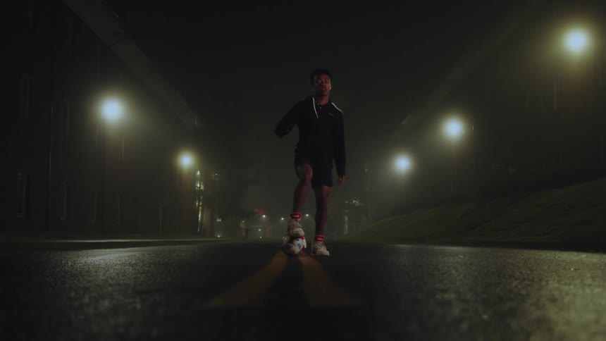 Boy dribbling a ball on wet asphalt at night