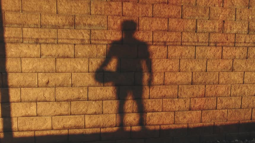 A soccer player holding a ball in silhouette against a brick wall