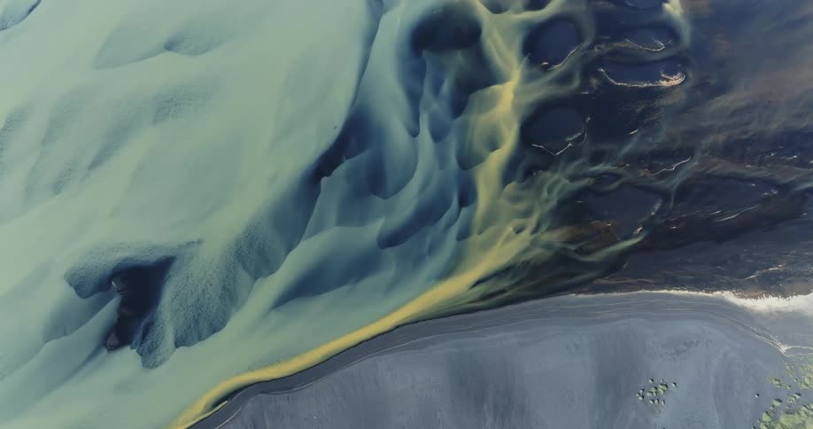 Aerial landscape of a light blue river meandering through dark sandbanks and green areas highlighting the natural patterns