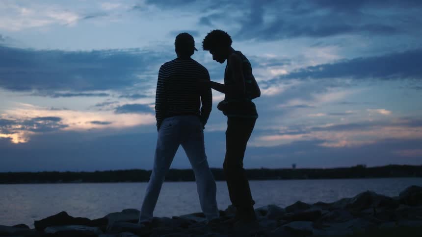 Two black men embrace while standing on a rocky coast