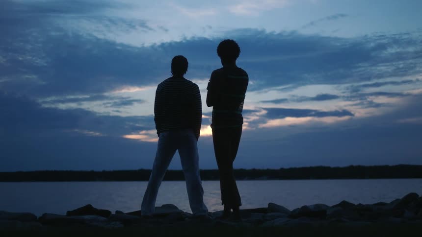Silhouette of two men in affectionate moment by the sea