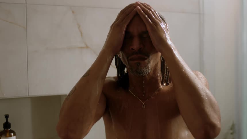 A man takes a bath in a shower water streaming down his body