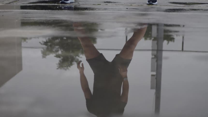 Reflection of a man stretching seen from a puddle of water on the ground