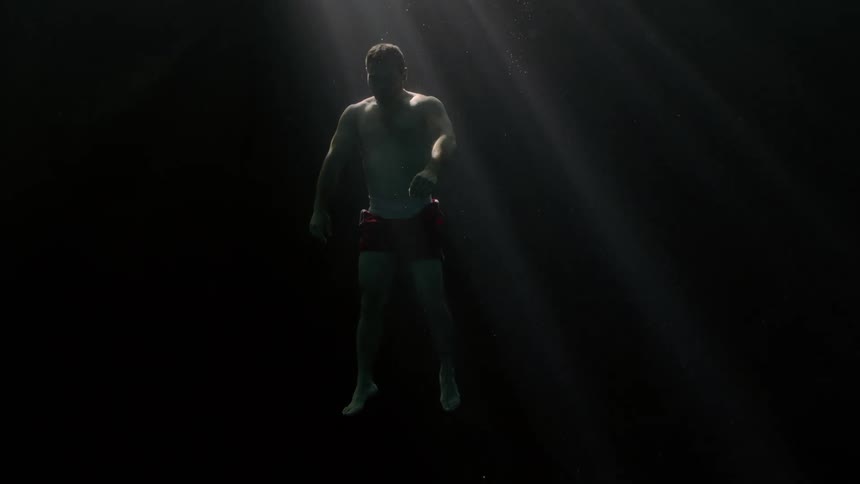 Man only in red swimming trunks descending into the ocean