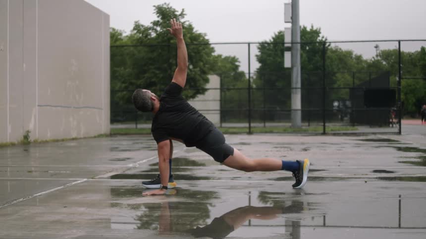 A man performs stretches on a wet tennis court
