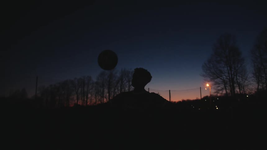 Silhouette of a boy doing tricks with a soccer ball outdoors at night