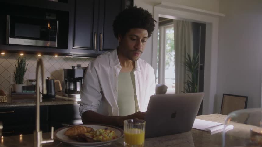 A man sitting down for a meal is using his laptop