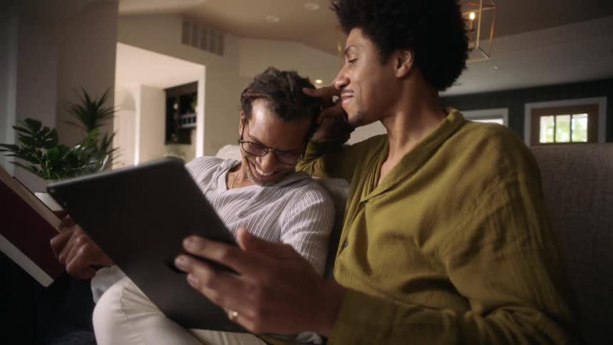Two males romantically flirt while laughing and sitting on a couch