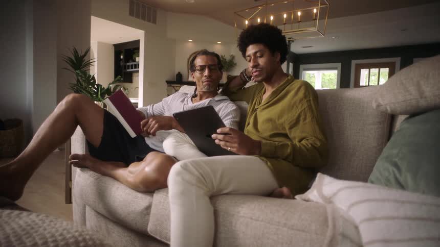 Two men sitting on the couch concentrating on a book