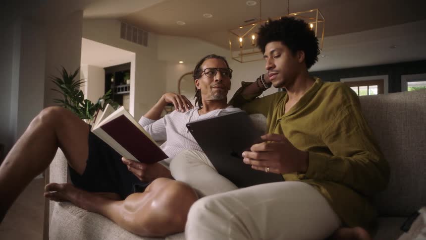 Two men sitting on a sofa reading a book