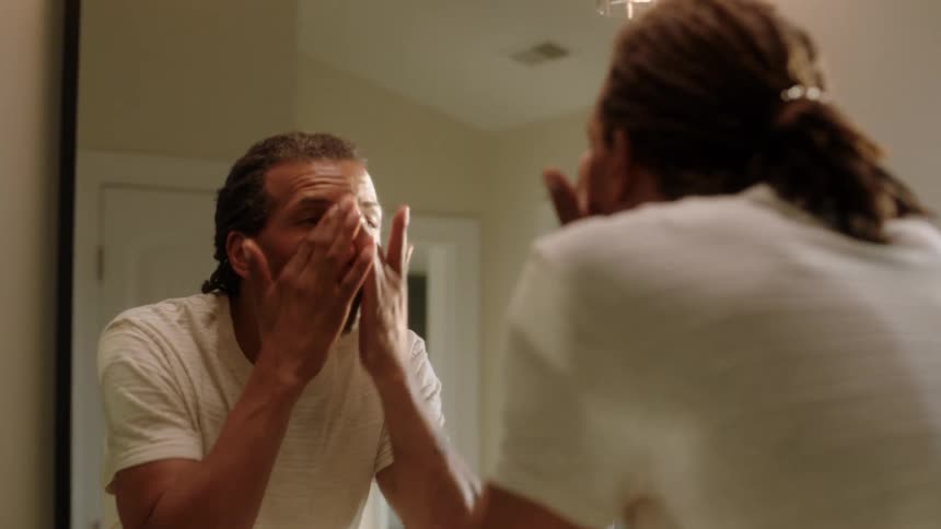 A man is wiping his face in the mirror
