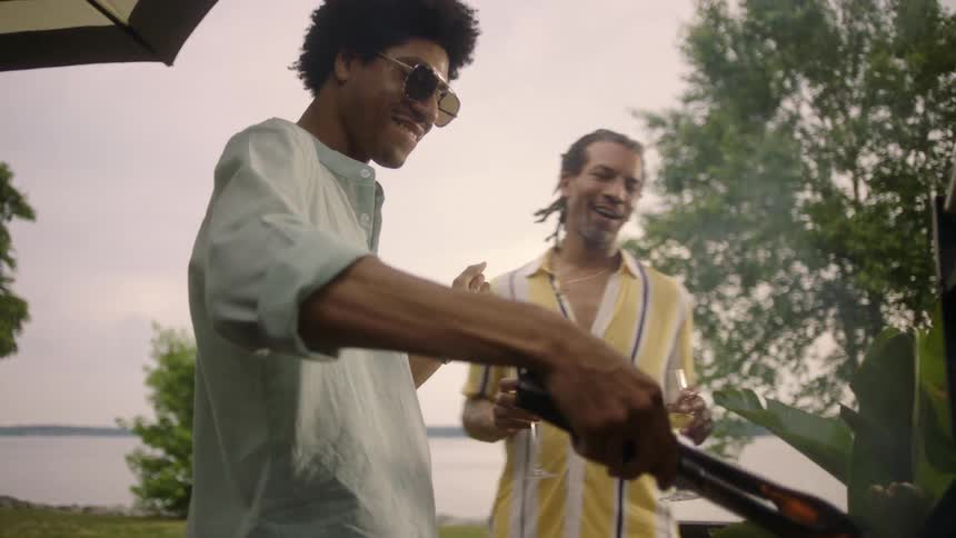 Two men joke around and laugh while having wine and grilling outdoors