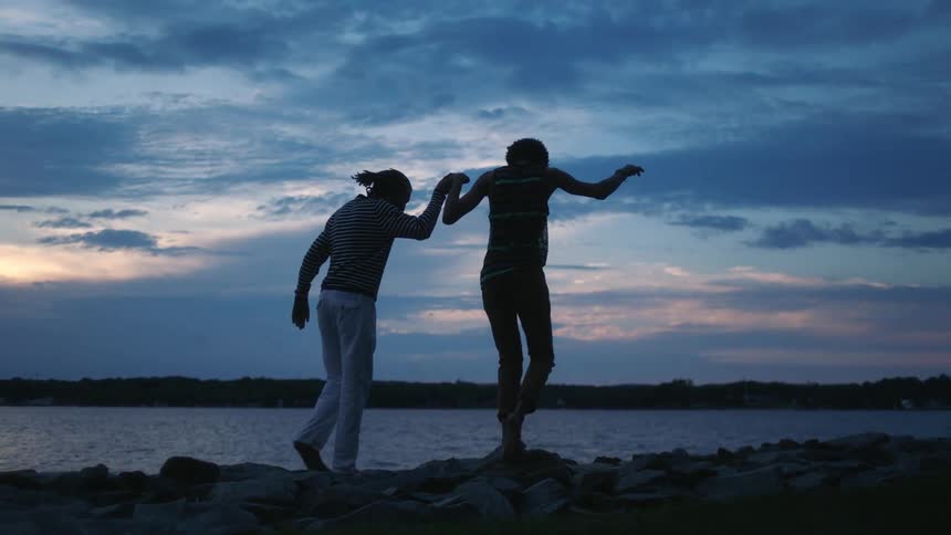 Two men hold hands while walking on the rocks