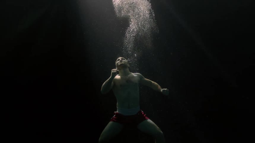 A person submerged in water swimming to the surface illuminated by a light source from above