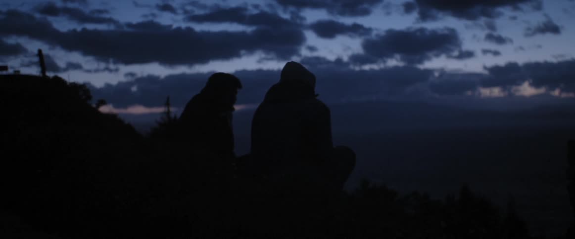 Two people stand outside near a fence in the dark