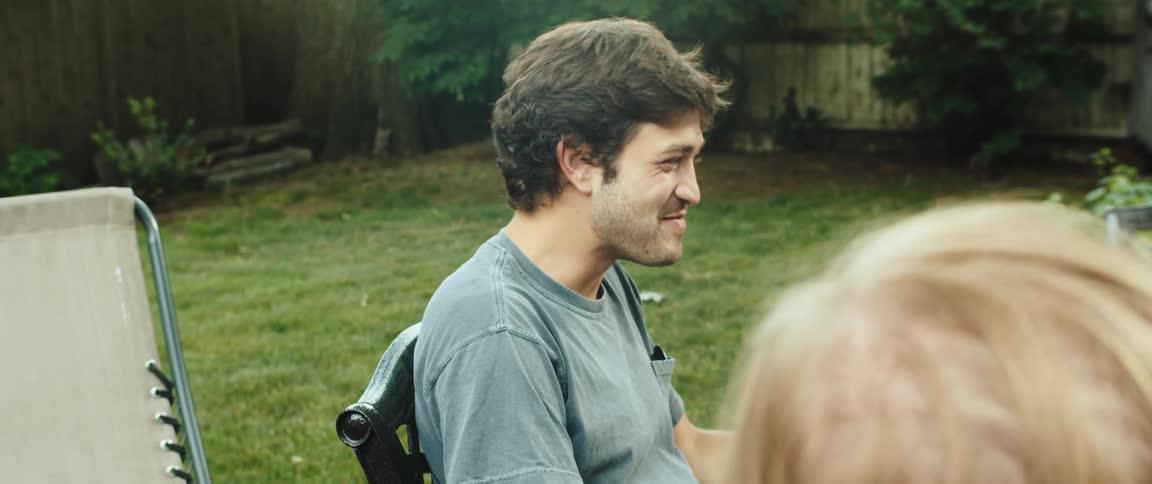 A happy young man smiles while looking at the camera sitting with friends in the backyard