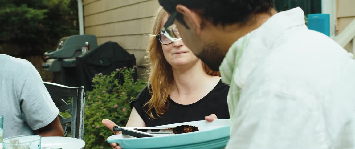 A woman hands a friend a plate of food outside