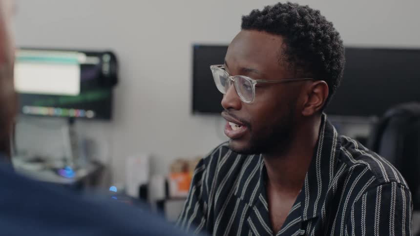 A black man converses with a white man in an office environment