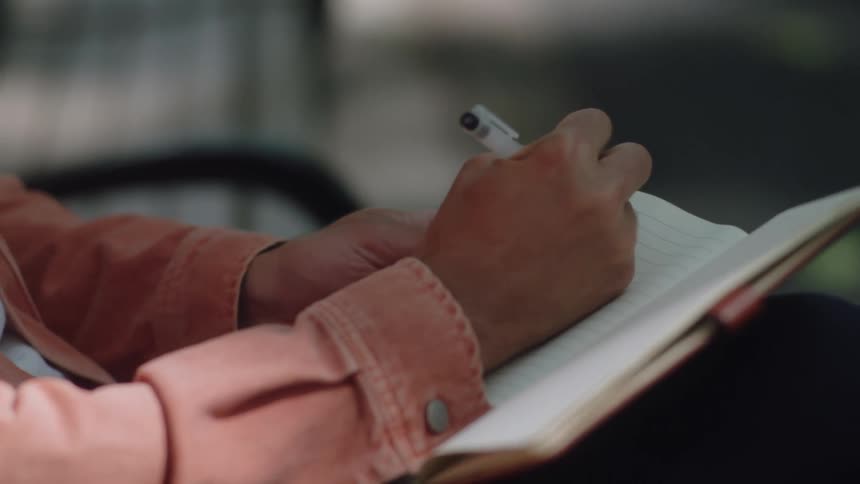 An individual opens a book and writes in it with a pen