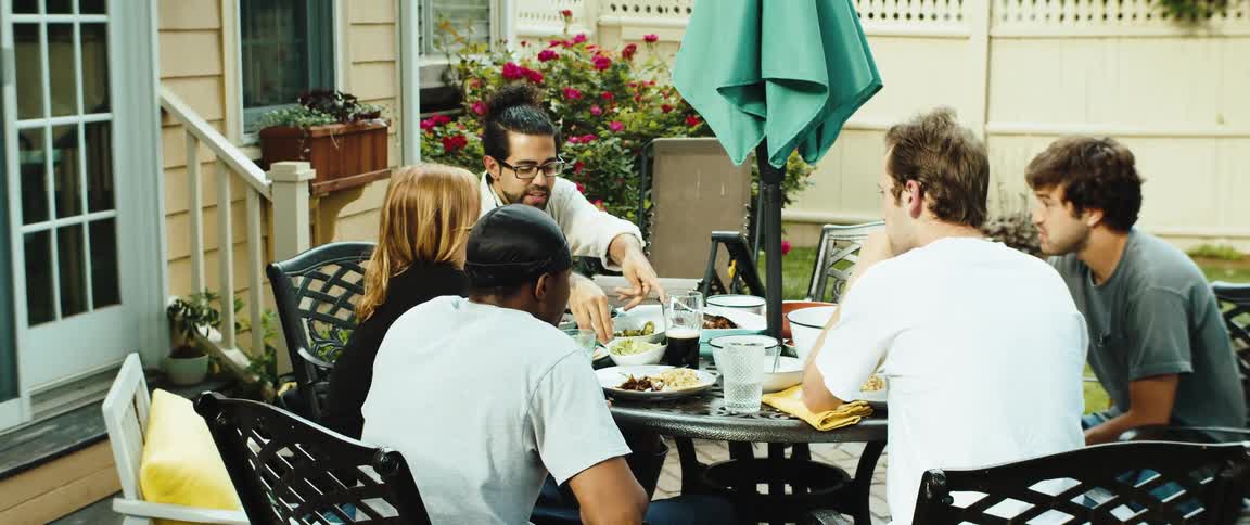 A happy group of friends sits around a patio table outdoors having lunch