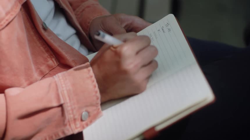 A closeup of a persons hand writing in cursive on a lined notebook with a pen