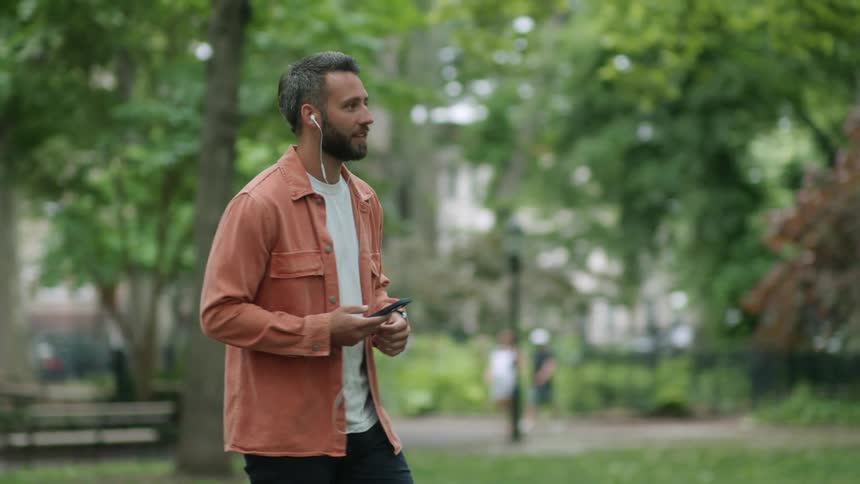 Man with cell phone and using a wired headset walking through the park