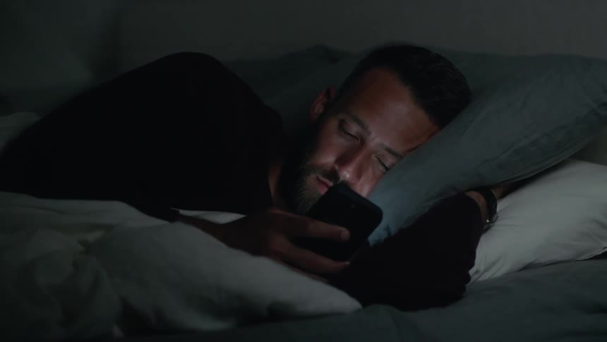Man lying in bed using his cell phone