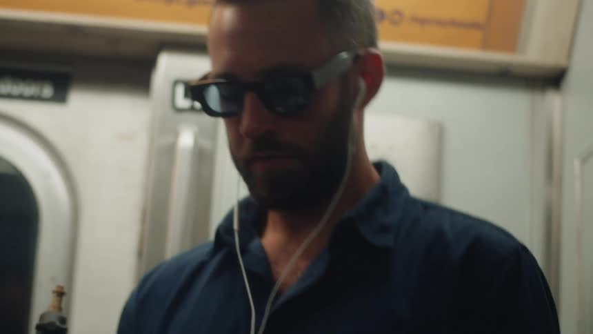 Man with sunglasses typing on a cell phone while inside a moving train