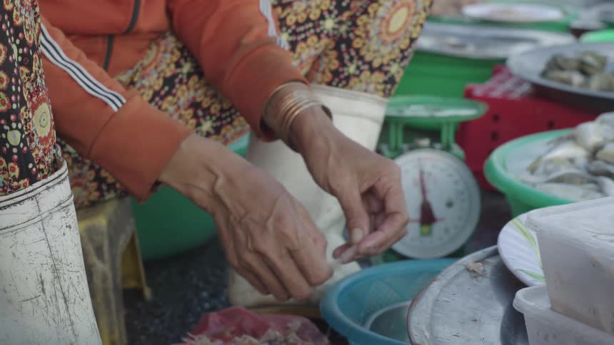 A woman pulls pieces of shrimp off at a marketplace