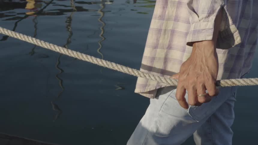 A closeup of a persons right hand gripping a thick rope near calm waters