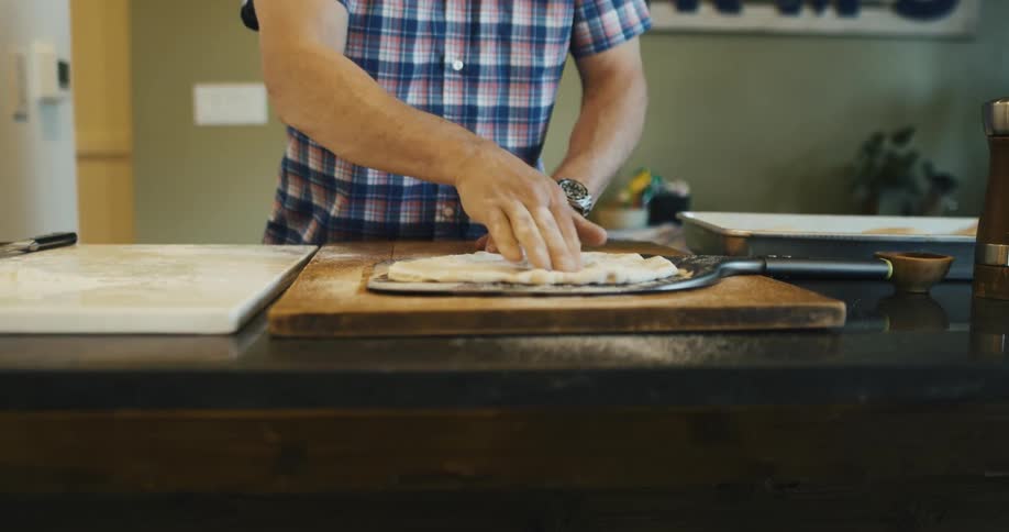 A man kneads pizza dough on a large spatula in a kitchen