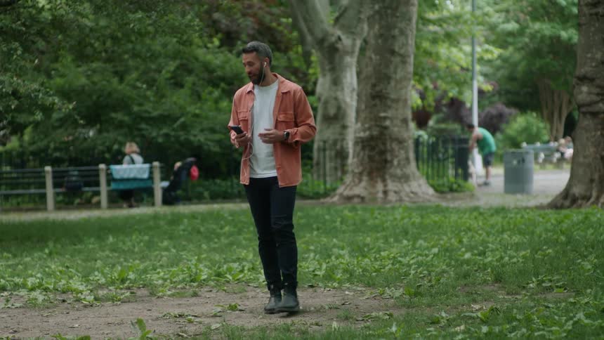 Man walking through a park while talking on his cell phone