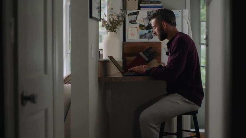 Man sitting typing on a laptop and using his cell phone