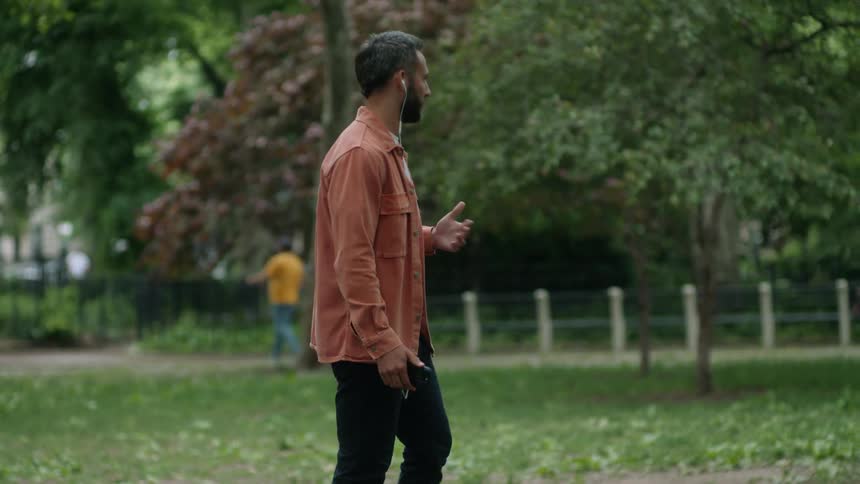 Man walking in a park while talking on the phone using headphones