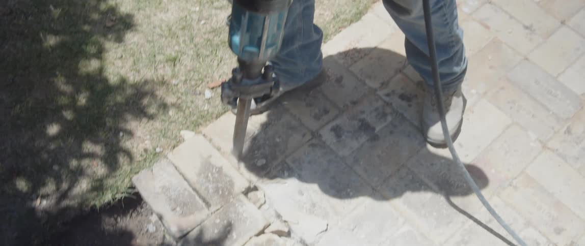 A person operates a blue jackhammer on a concrete surface surrounded by debris
