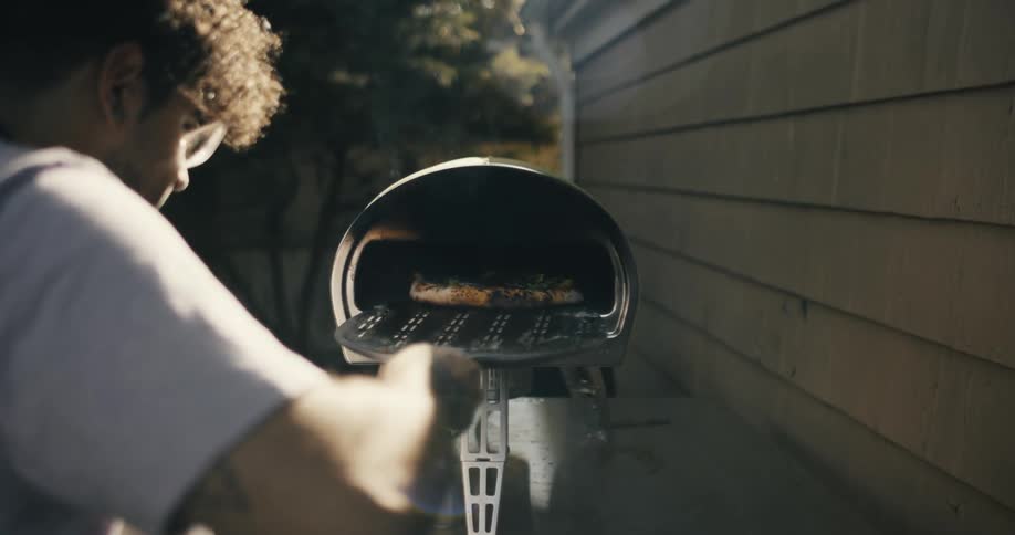 A Dominican man cooking pizza in a pizza oven