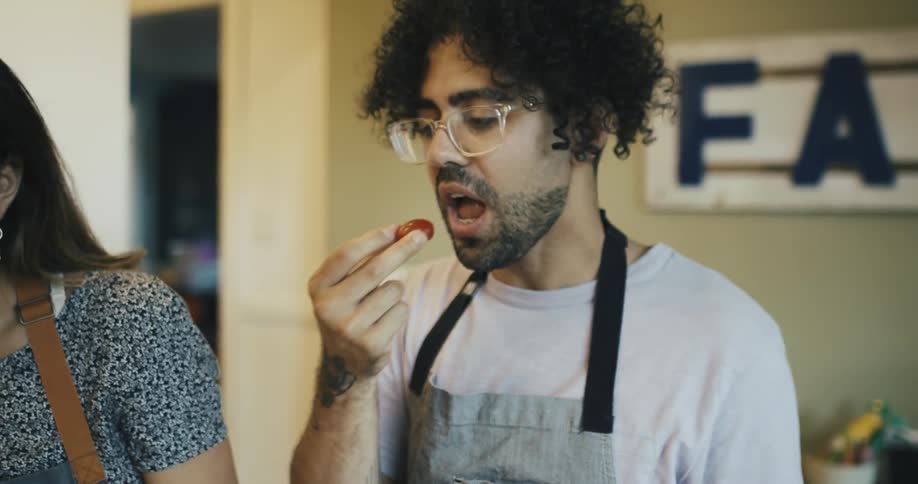 A young man in an apron cooking with his girlfriend
