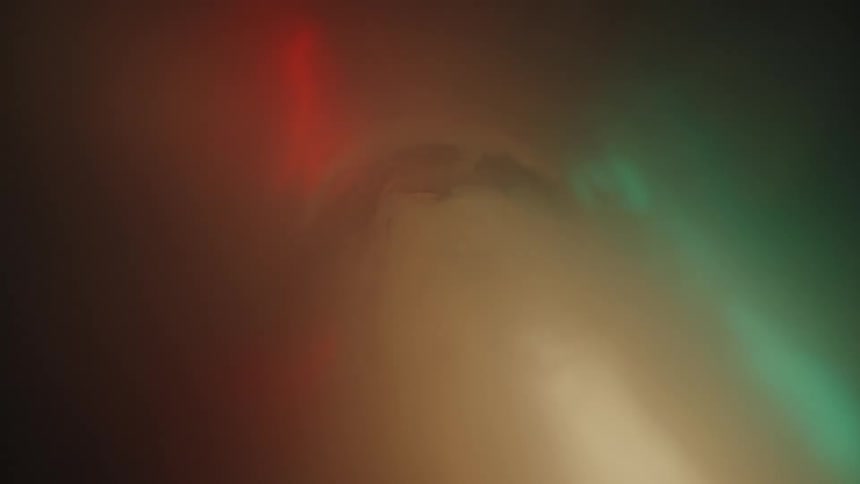 The interior of a semi translucent plastic tube with green and red lights reflecting on its walls filling with smoke