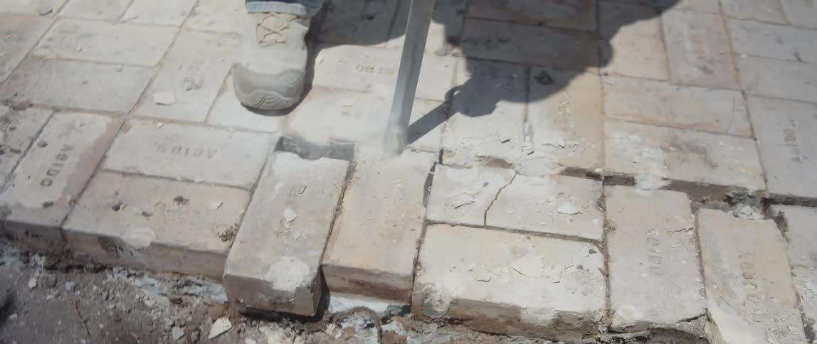 A worker in heavyduty boots operates a jackhammer breaking up concrete