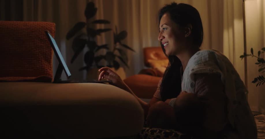 A woman sitting on the floor of the living room at night working on a laptop