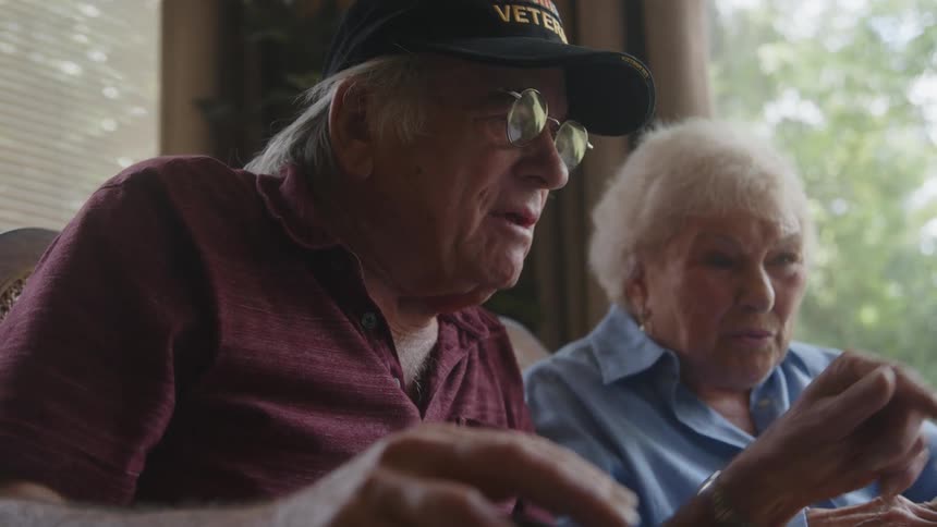 Two smiling elderly people sitting side by side talking