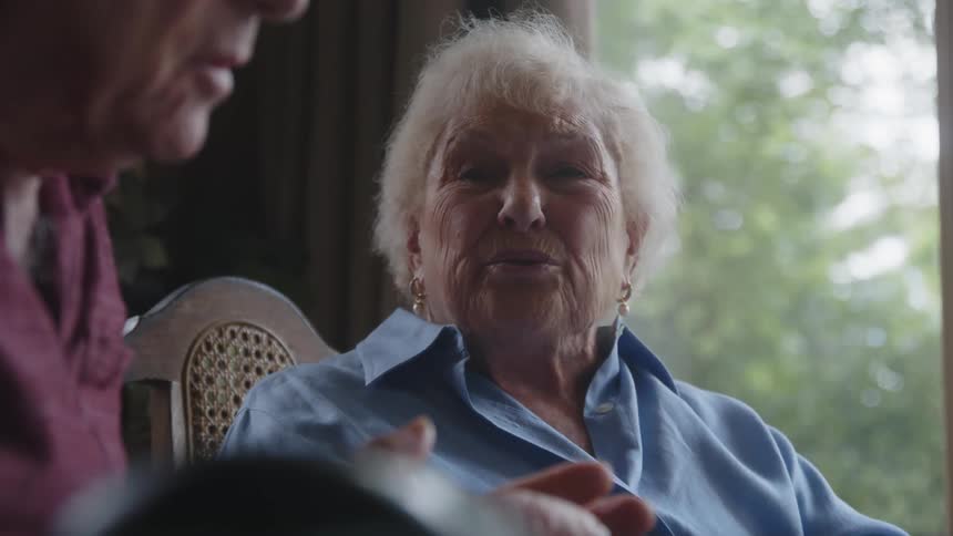 Two elderly people sitting at a table talking to each other