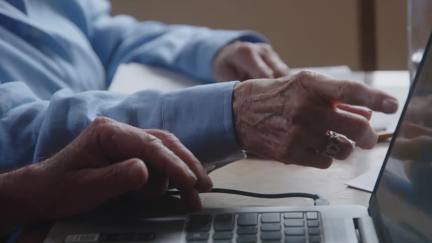 Two elderly hands pointing at a laptop