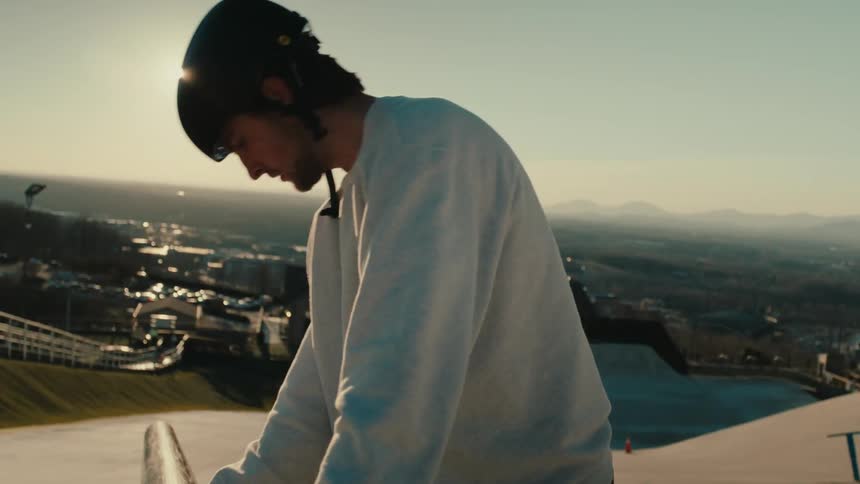 A person in a white sweater wearing a helmet polishes a metal railing on a ski ramp