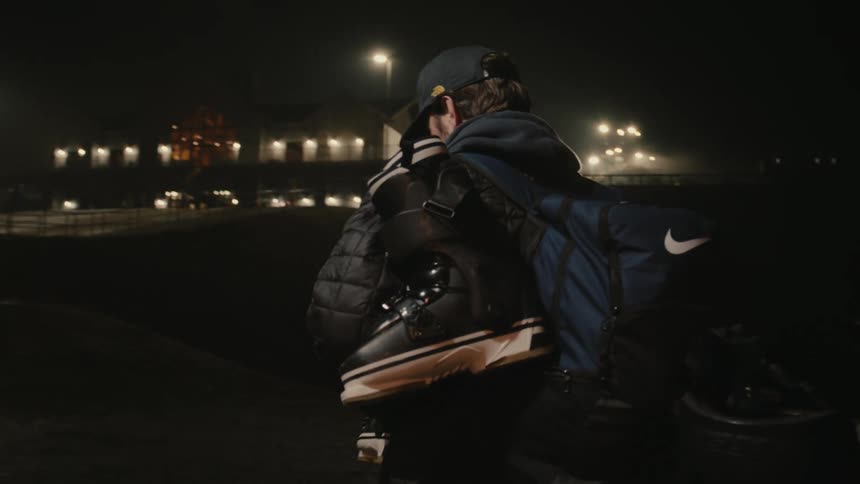 A man walks through a door heading outside carrying hockey equipment
