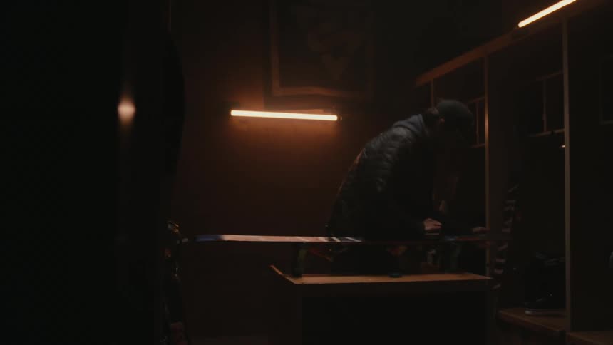 Man leaning over a table in a dark environment lit by a light cleaning a ski equipment