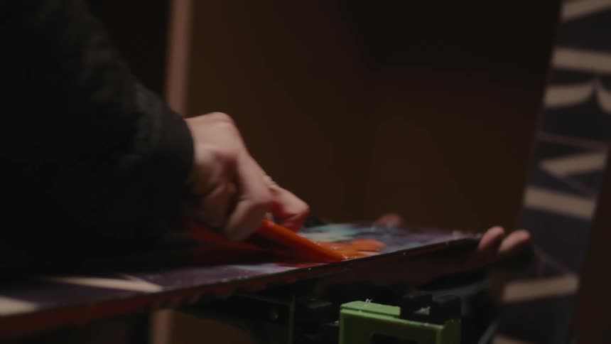 Close up of a hand using a plastic spatula to clean debris from the surface of a ski