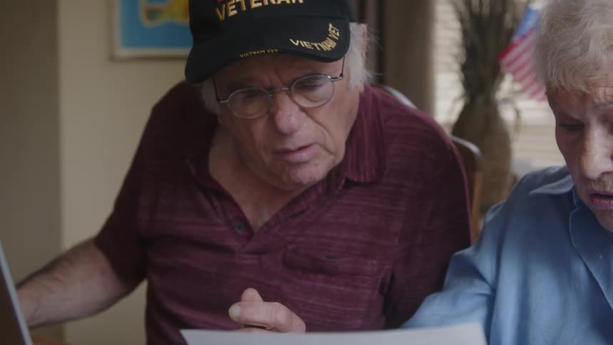 Elderly couple sitting at a table analyzing documents next to a laptop