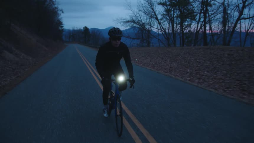 A man rides a bicycle down a remote road at dusk